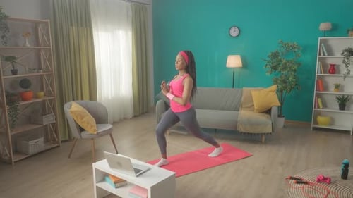 Una mujer afroamericana haciendo estocadas hacia adelante con los brazos levantados por encima de la cabeza Una mujer joven