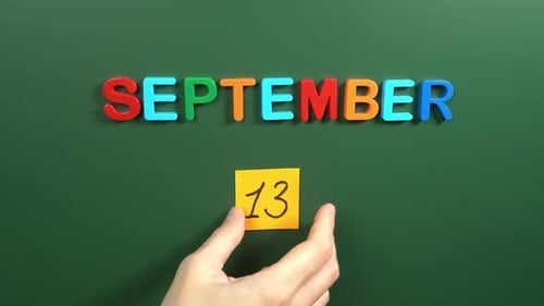 Hand sticking a sticker 13 September calendar day on school board. 13 date of September. Thirteenth