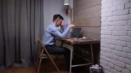 Tired Young Man Working at Desk on Laptop