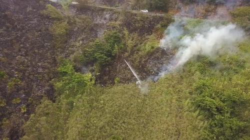 Firefighter putting out vegetation fire, cars passing on road in background. Aerial