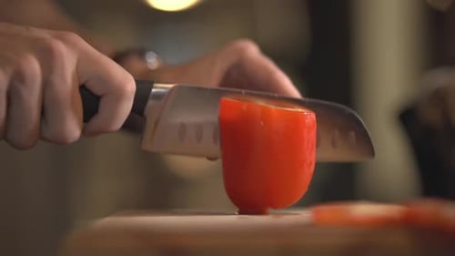 Person Using A Stainless Knife And Cutting A Red Bell Pepper Into Half. - close up