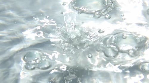 Klarer Wasserstrahl, der in hellem Licht mit Blasen plätschert