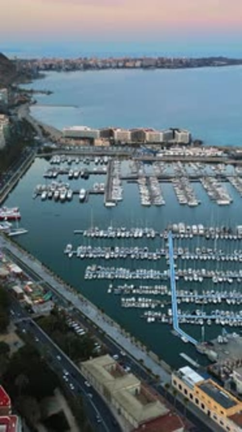 Aerial drone view of the Port of Alicante and the buildings in the city in the evening. Vertical