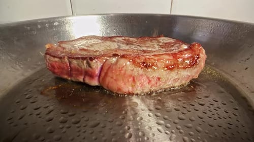 Close-up of a Delicious Juicy Steak Sizzling in a Hot Pan for a Gourmet Meal