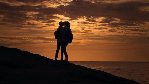 A Couple Standing on Top of a Hill Overlooking the Ocean at Sunset