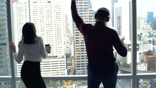 Businesspeople Listening to Music and Dancing by Window in Office Apartment