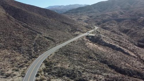 Wüstenberglandschaft mit kurvenreicher Straße und fahrenden Fahrzeugen, Luftaufnahme