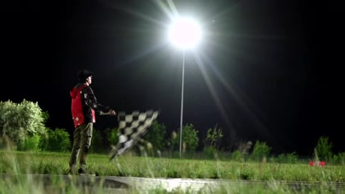 Un maréchal de course de nuit brandissant un drapeau à damier sous un projecteur, des traînées de karting floues après l'arrivée