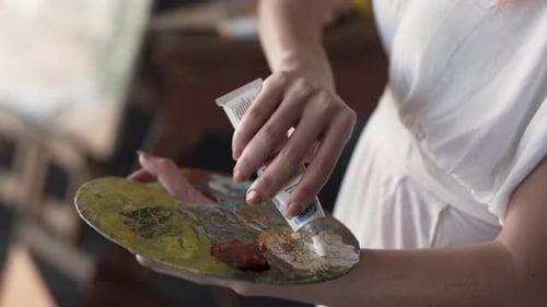 Nahaufnahme einer Malerin, die Farben aus einer Tube auf einer Palette mischt. Frau ist Painti