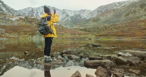 Photographer Standing on Rocks By Mountain Lake Enjoying Landscape