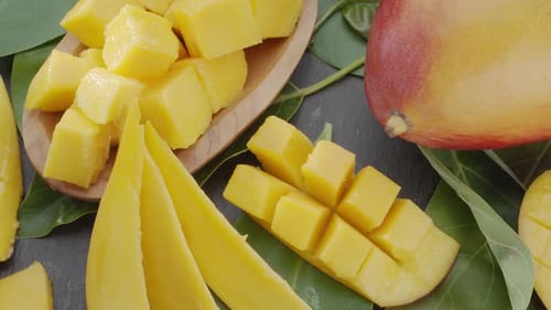 Mango fruits with slices and mango leaves slowly move in the frame on a gray stone table.