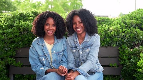 Twin Sisters Sitting and Smiling on Bench in Park