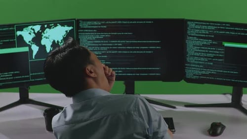 Back View Of Tired Asian Man Yawning While Write Code With Multiple Computer Screens In Green Screen