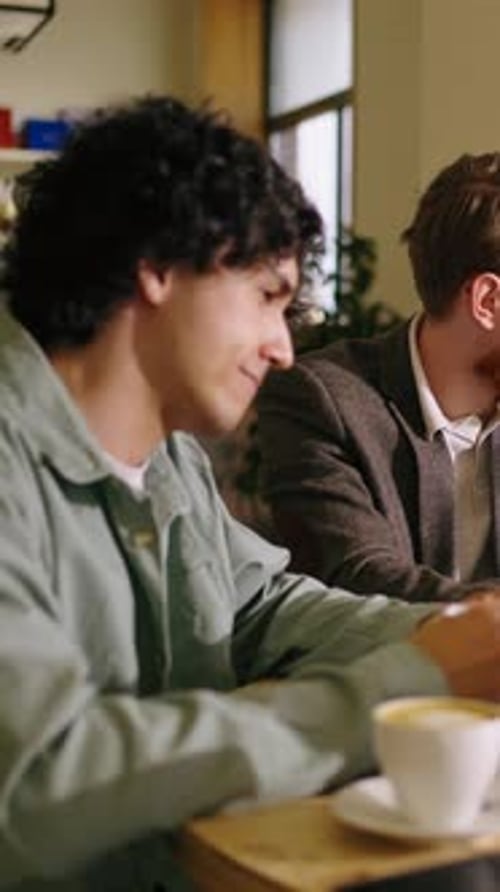Focused Young Professionals Collaborating at a Cozy Cafe Table Reviewing Documents and Digital