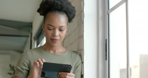 A young African American woman browses her tablet by a window