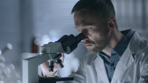 Scientist Analyzing Sample Through Microscope in Laboratory