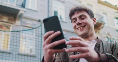 Close Up of Young Handsome Joyful Caucasian Man Standing at Street and Using Smartphonet Outdoor