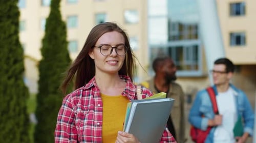 Outdoor Portrait of Attractive European College Girl in Striped Shirt Holding Her Belongings Smiling