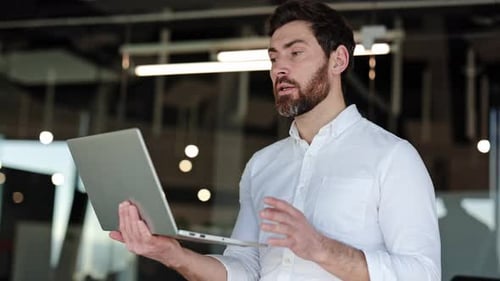 Bearded Businessman Having Video Call on Laptop in Modern Office