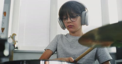 Boy with Headphones Plays Drums Indoors