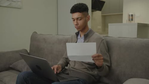 Young Man Working on Laptop, Reading Documents on Couch