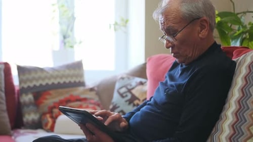 Senior Man Relaxing on Couch Using Tablet Device
