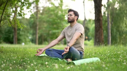 Young adult sports man meditating barefoot sitting in the lotus position on mat in an urban city