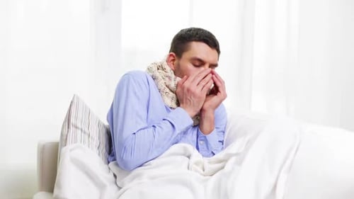 Man with cold blows nose while lying in bed