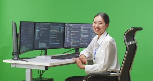 Woman Developer Smiling To Camera While Write Code With Multiple Computer Screens In Green Screen