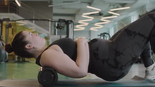 Woman Exercises Back With Foam Roller in Gym
