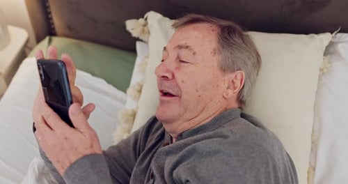 Older Man Laughing and Talking on Phone in Bed