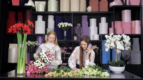 Two Female Florists Standing at a Table in Flower Workshop Holding a Bouquet of Flowers and Mixed