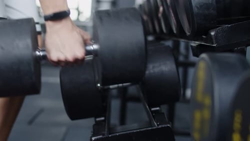 Male hand bodybuilder takes dumbbells from rack in gym, closeup, side view. Male powerlifters hand t