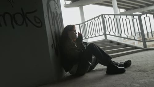 Woman Sitting Somberly Against Wall and Rubbing her Face in Distress