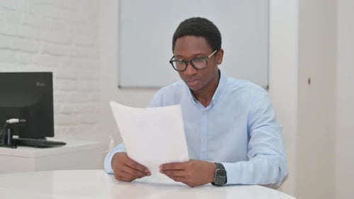Young Adult Reviews Documents at Desk in Office