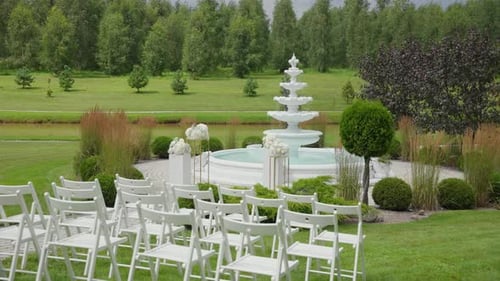 Beautiful outdoor wedding ceremony setup featuring white chairs and a decorative fountain,