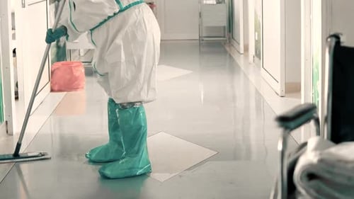 Lower shot of janitor mopping hospital floor in covid-19 protective gown and booties