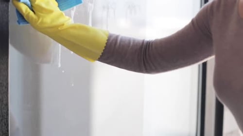 Woman Cleaning Glass Surface with Gloves and Cloth