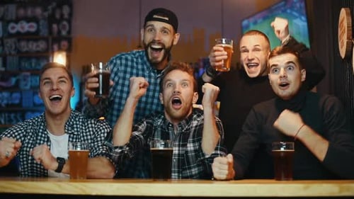 Celebrating victory, knocking glasses. Group of soccer fans together indoors in the pub have fun
