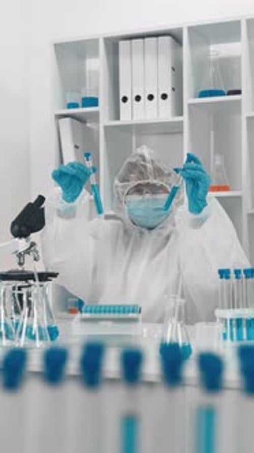 Un científico con traje protector lleva a cabo un experimento de laboratorio con un líquido azul en tubos de ensayo