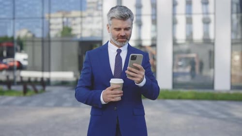 Cheerful Entrepreneur Handsome Bearded Guy Is Walking in the City Using a Mobile Phone Holding