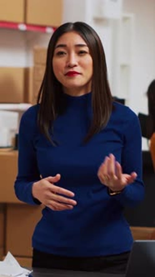 Woman Speaking in Workplace with Boxes Behind Her