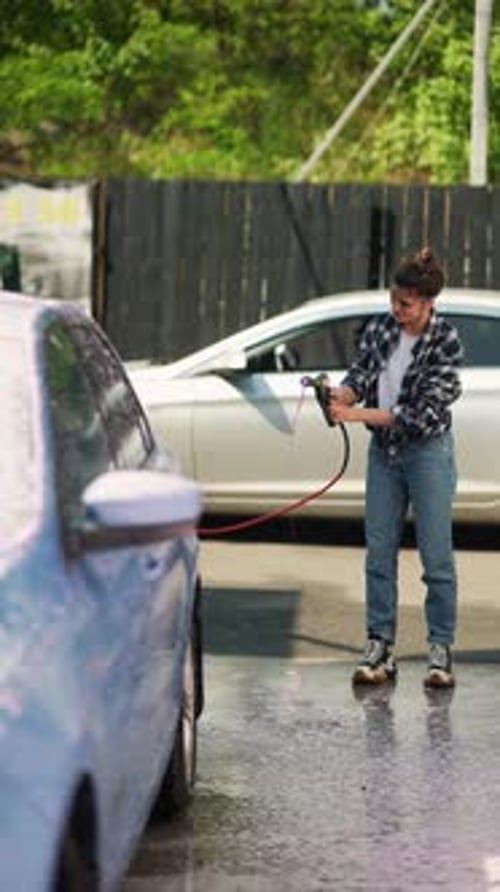 At the Car Wash a Vibrant Young Lady is Enthusiastically Cleaning Her Car with a Foam Gun