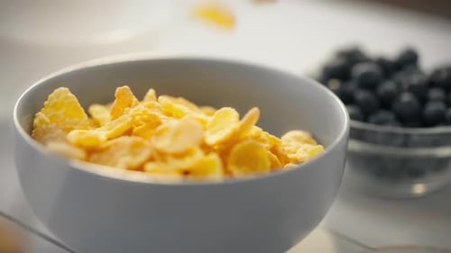 Dieter preparing breakfast by filling a plate with cornflakes. Slow motion of yellow corn grains