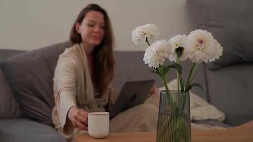 Woman Works on Laptop, Drinks Coffee at Home
