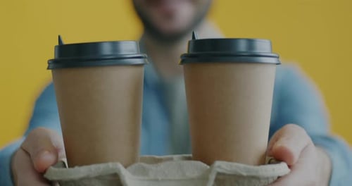 Gros plan de mains masculines déplaçant des tasses à café à emporter vers la caméra livrant une boisson sur fond jaune