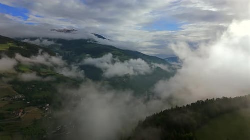 A stunning aerial view of a mountain valley partially covered in fog and clouds, revealing glimpses