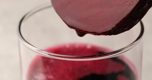 Dripping beetroot juice from piece of fresh beet into glass against light background, closeup