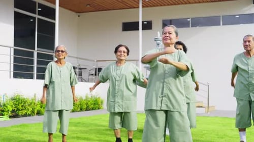 Group of senior or elderly Asian man and woman exercise together on grass field in front of building