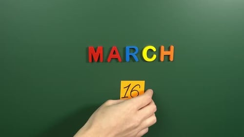 Hand sticking a sticker 16 March calendar day on school board. 16 date of March. Sixteenth day